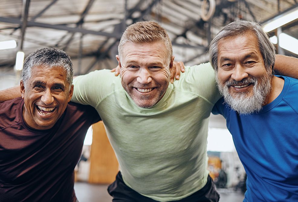 3 older guys huddled together looking at the camera smiling